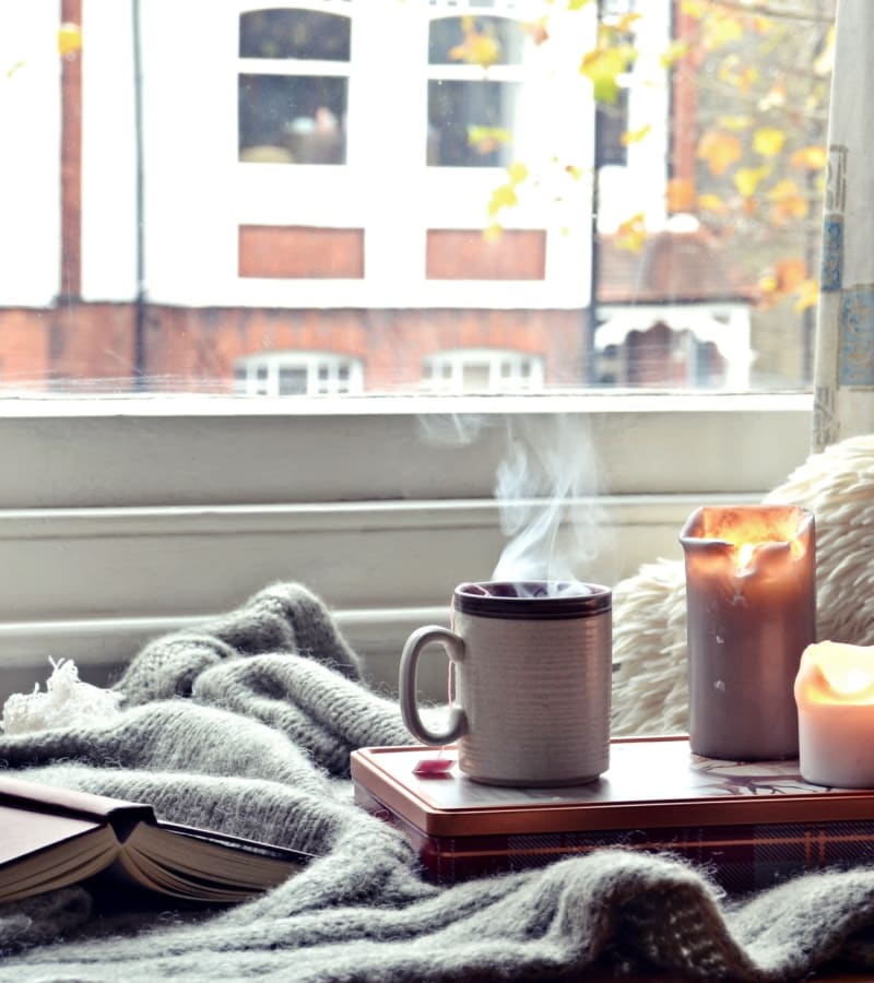 Cozy blanket, book, coffee, and a candle set up next to a window at Parkside Towns in Richardson, Texas