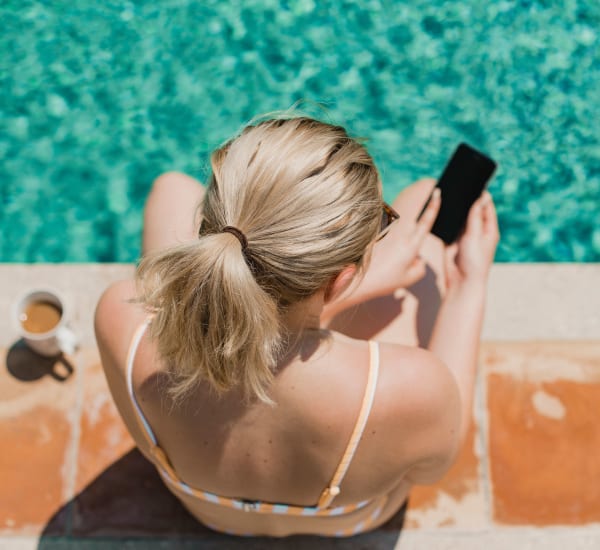 A woman sitting on the edge of the pool using her phone at Mode at Hyattsville in Hyattsville, Maryland