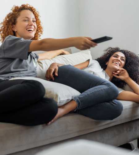 Friends lying on the couch and watching tv atRoosevelt Park Apartments in San Jose, California