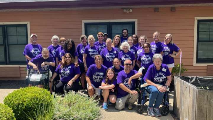 Residents and staff standing outside wearing purple shirts smiling for a group photo