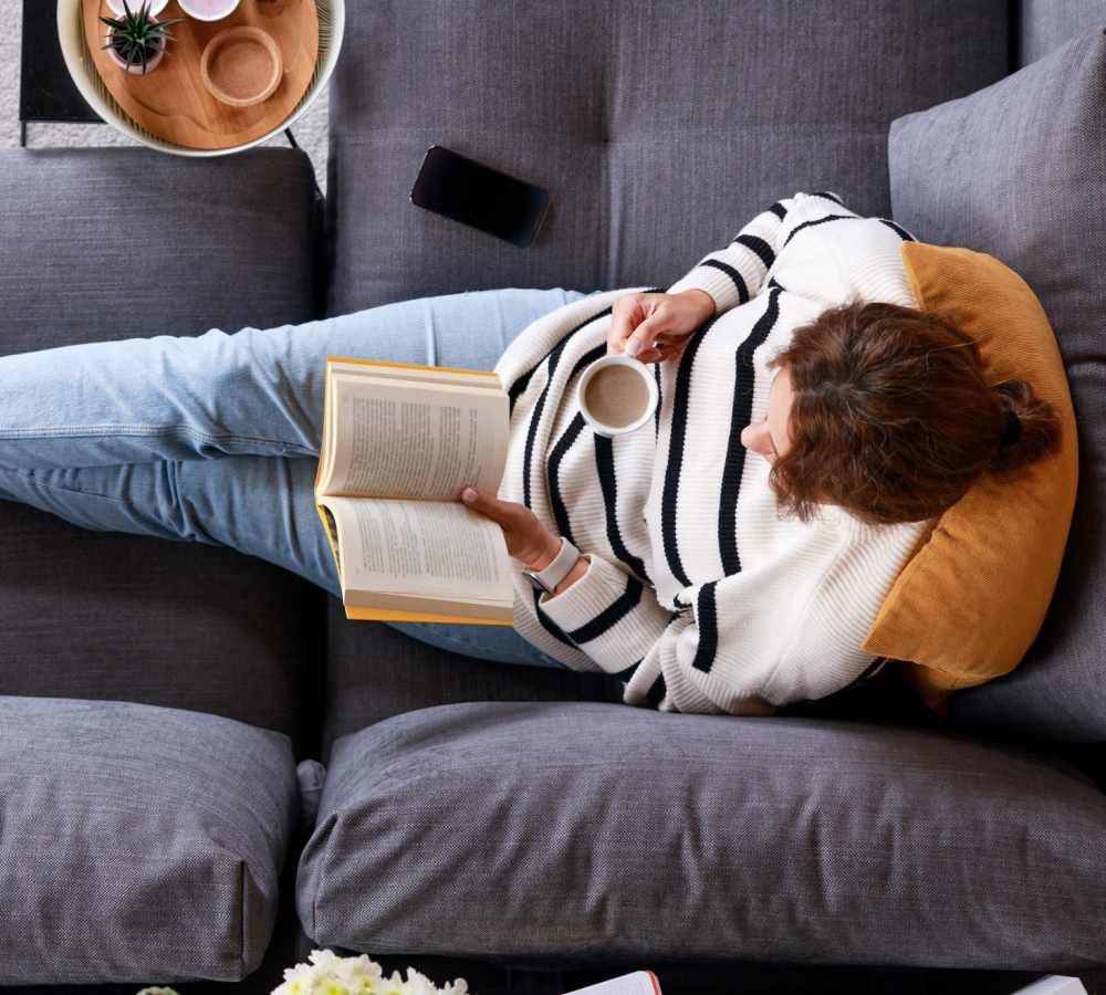 Resident reading book on couch while drinking coffee at Polly O'Meara Doyle Hall in Santa Rosa, California