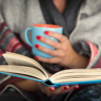 A woman holding a cup of coffee and reading a book at The Station at Clift Farm in Madison, Alabama