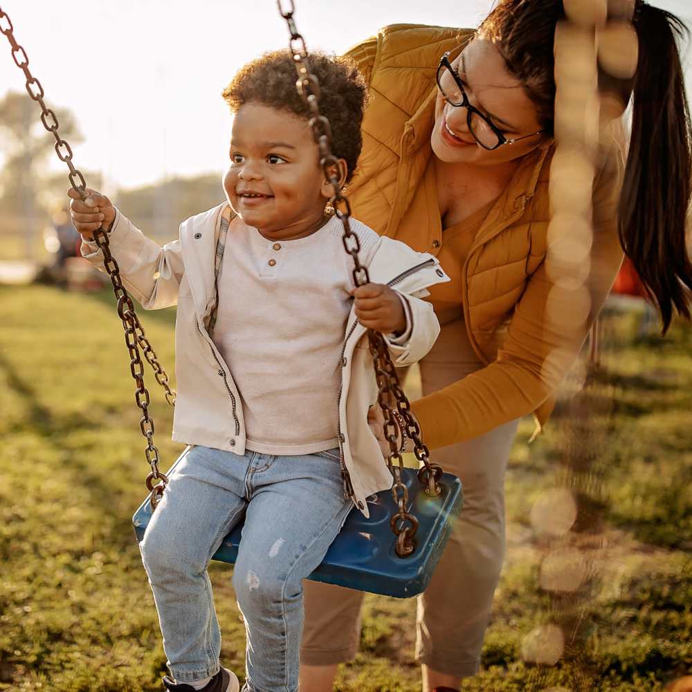 Happy resident pushing a child on a swing at Rich Park Apartments in Raleigh, North Carolina