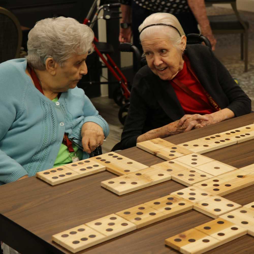 Two memory care residents enjoying conversation while playing oversized dominoes at Watermere Frisco.