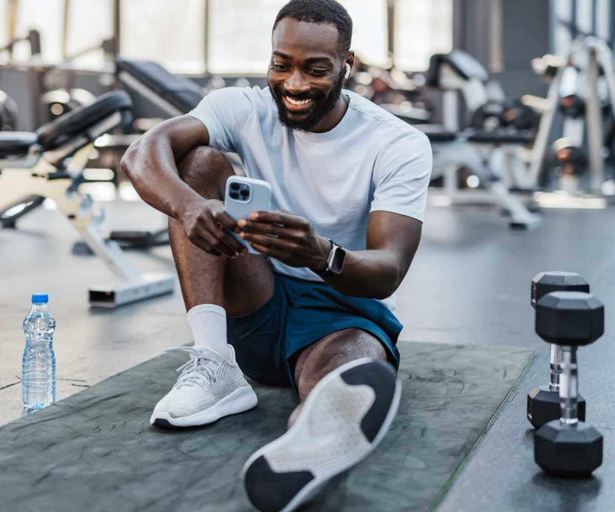 A man seated on the gym floor, focused on his phone at Sadler House in San Marcos, Texas