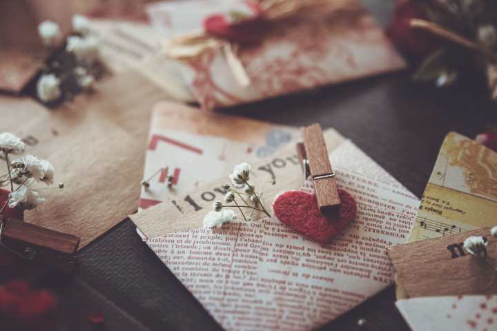 folded newsprint envelopes with handmade felt hearts and baby's breath flowers attached to envelopes with wooden clothes pins, sprad on a solid surface. 
