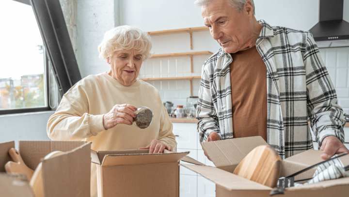 A senior couple packs kitchen items into boxes as they prepare for their move to a senior living community.