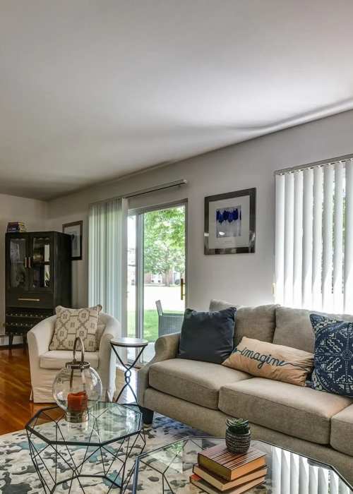 Cozy living room with couch, chair and glass door leading to balcony at Park Ridge Commons in Des Plaines, Illinois