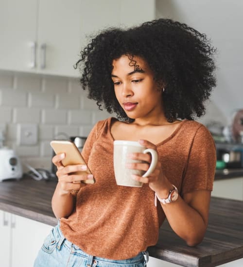 Resident surfing the web on her phone while enjoying morning coffee in her new home at Magnolia Heights in San Antonio, Texas