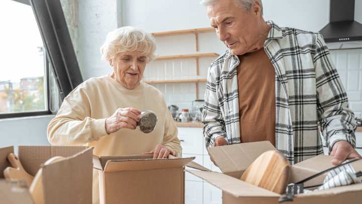 A senior couple packs kitchen items into boxes as they prepare for their move to a senior living community.