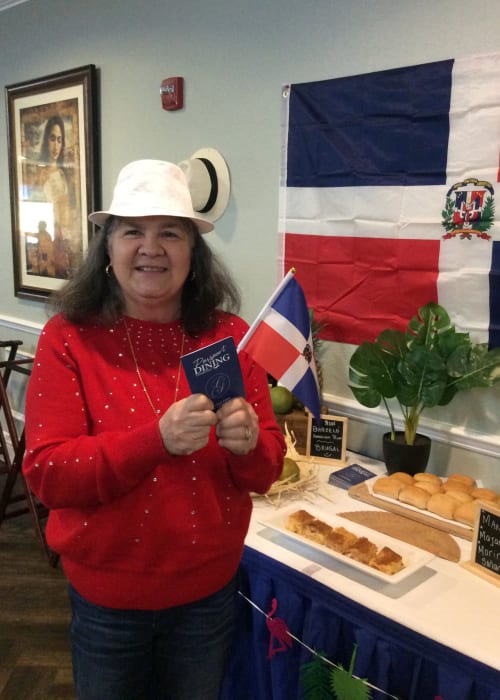 Resident posing for a photo in front of international dishes at a passport dining event at Grand Villa of Delray West in Delray Beach, Florida