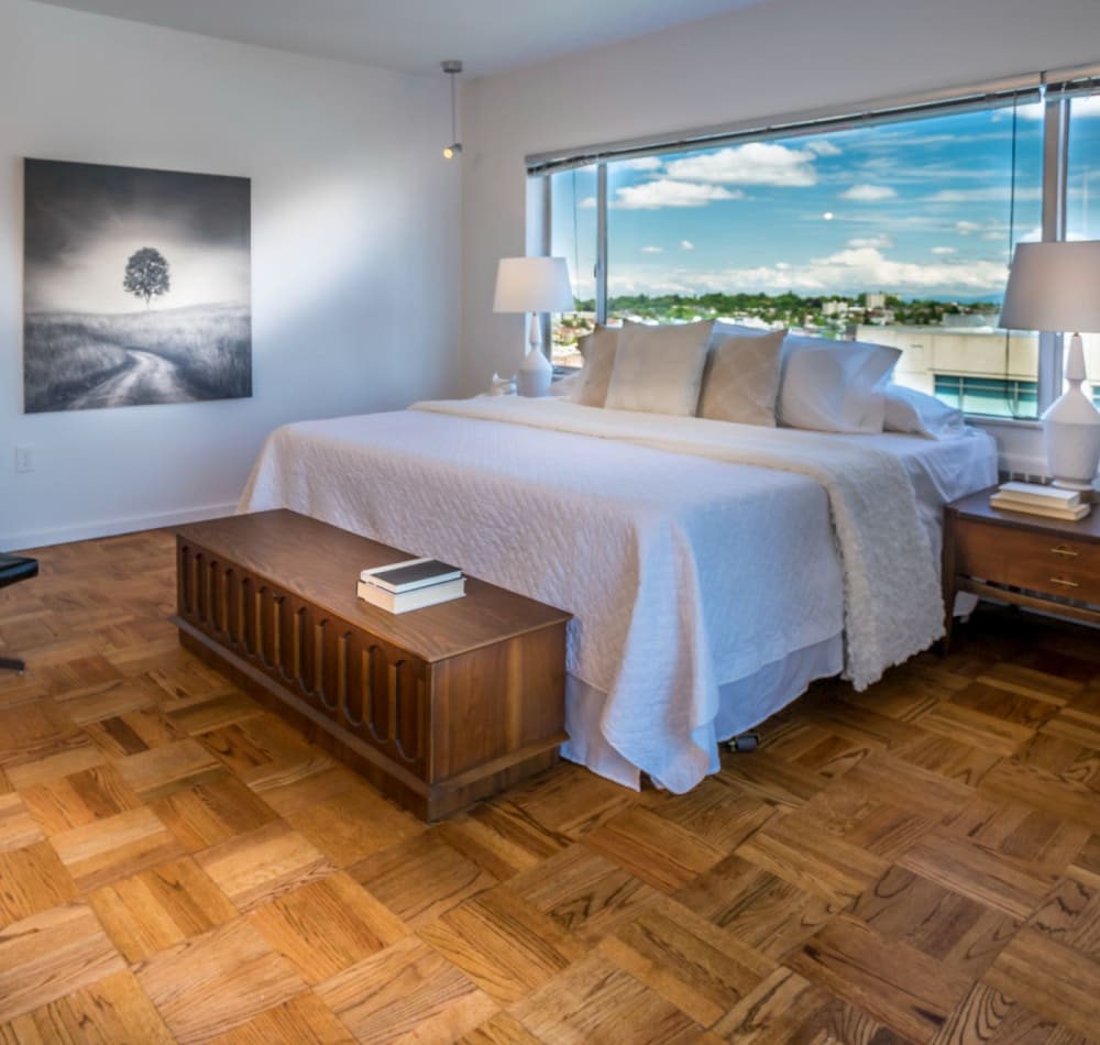 Well-furnished model home's primary suite with floor-to-ceiling windows and a terrific view of the city at Panorama Apartments in Seattle, Washington