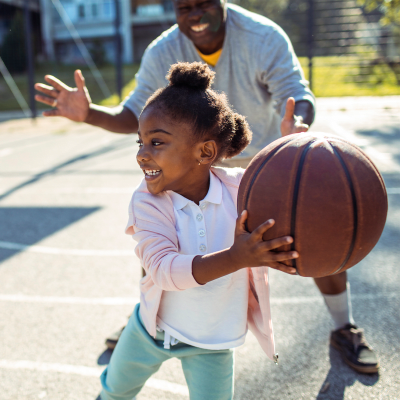 A father and daughter playing basketball on a court at Carl Vinson Park in Lemoore, California