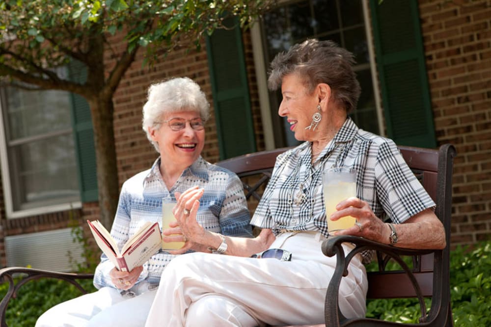 Two seniors talking while sitting on a bench outside at The Birches at Harleysville in Harleysville, Pennsylvania