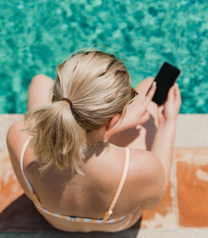 Resident using their phone while sitting next to the pool at Apple Creek Apartments in Stillwater, Oklahoma