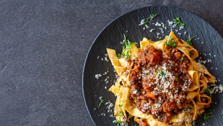 Overhead view of a delicious bolognese sauce served with pasta and parmesan cheese on a dark plate on black table background. | Italian Restaurants in Savannah