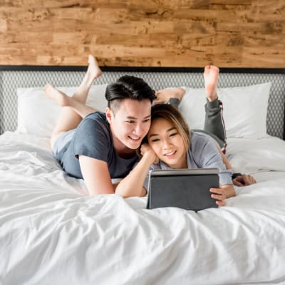 Two residents laying on a bed looking at a tablet at Meriwether Landing in Joint Base Lewis-McChord, Washington