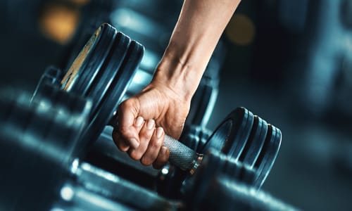 Resident picking up a weight in the fitness center at Trinity Way in Fremont, California