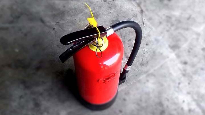 Fire extinguisher with black hose and yellow safety pin on a concrete floor