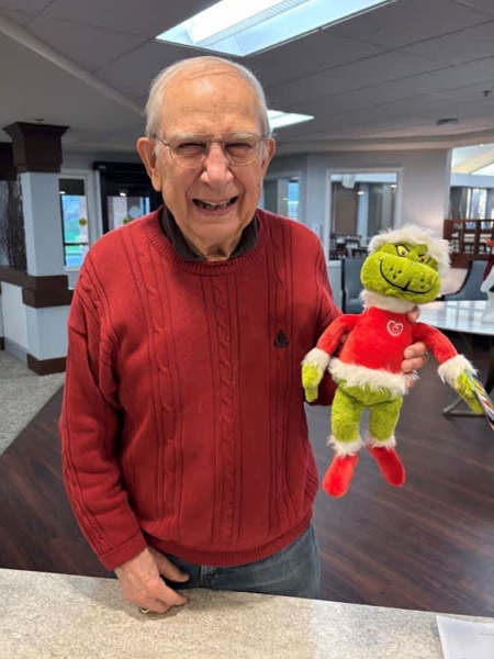Cheerful resident posing with a Grinch plush doll