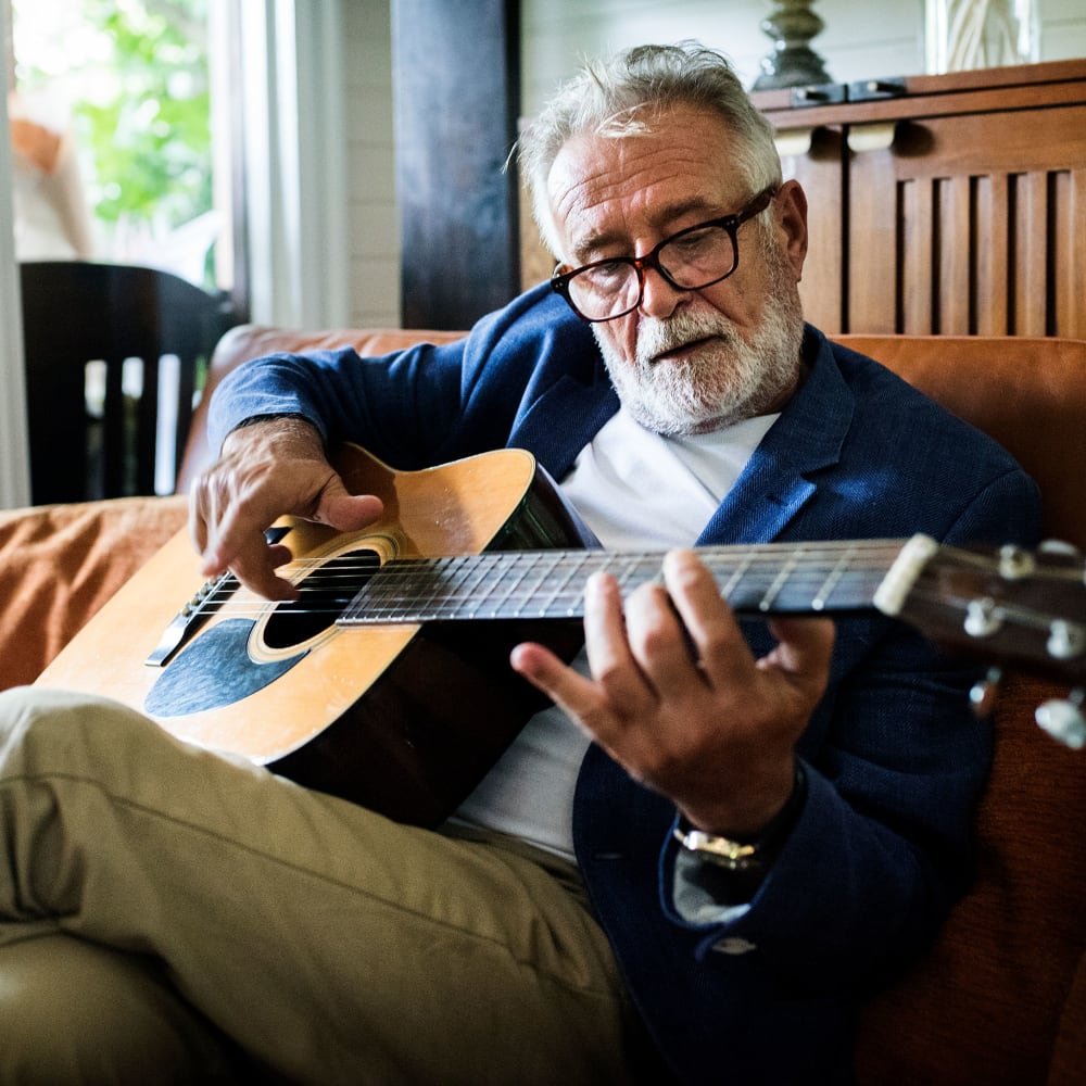 Senior man playing a guitar at Randall Residence at Encore Village in Brighton, Michigan