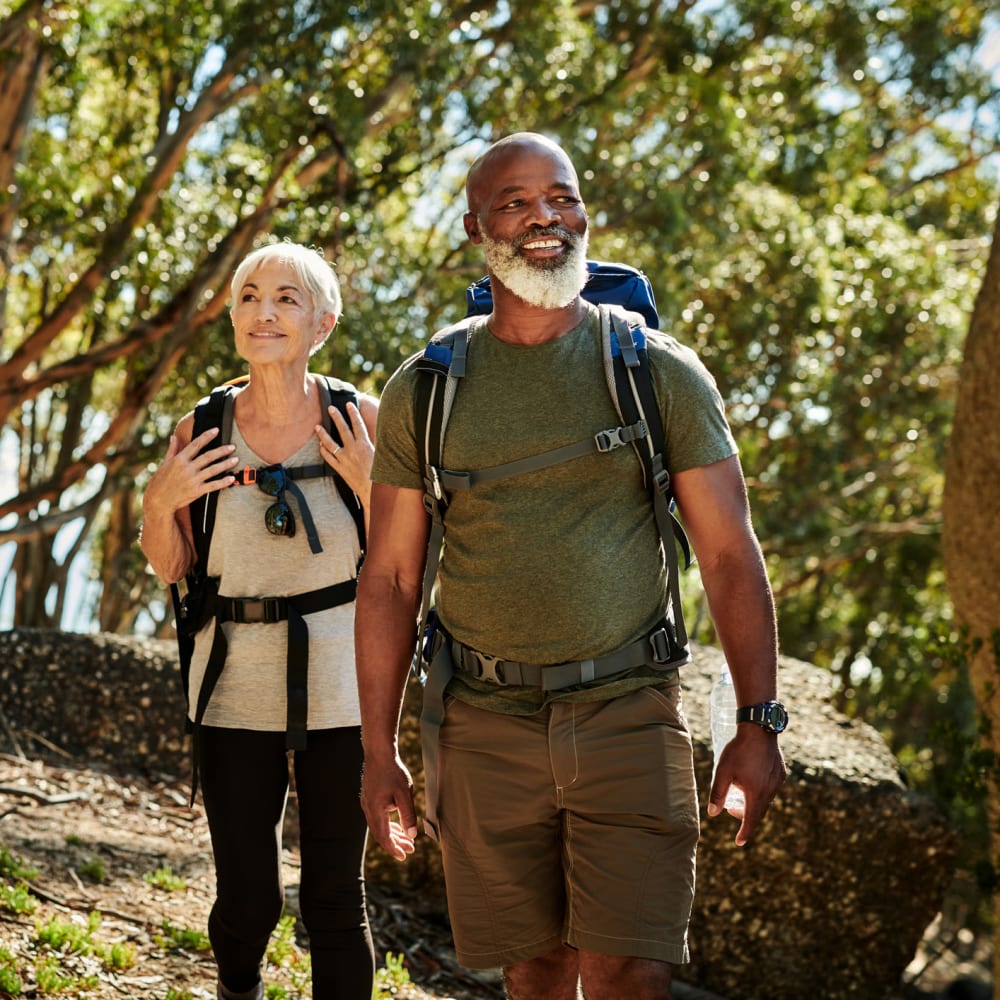 Resident couple on a light hike through a lush forested area near our Village Green Senior community at Mission Rock at Sonoma in Sonoma, California
