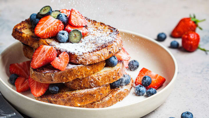 A pile of French toast with blueberries, strawberries and powdered sugar on a white plate | French Toast in Chandler