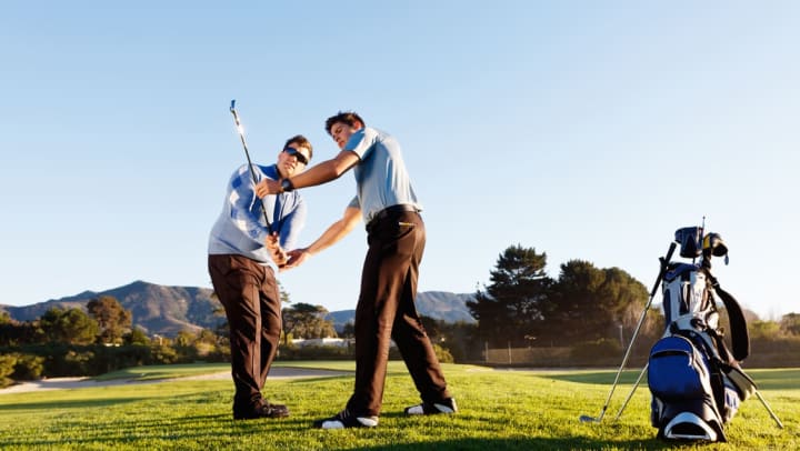 A golf coach helping an older man practice swinging at a golf course | Golfing Lessons in Pompano Beach