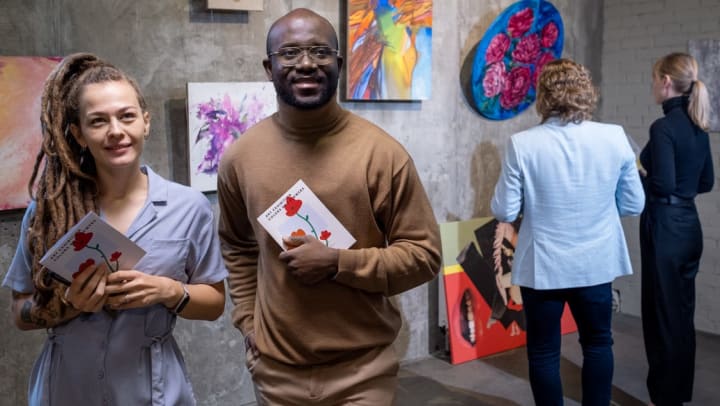 a man and woman holding gallery pamphlets look at art in the distance with a wall of art behind them | art gallery near Raeford