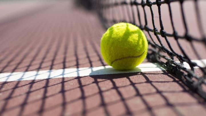 a tennis ball sitting next to the net that is casting a shadow on the tennis court | tennis lessons around Irvine