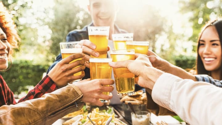 Young people smiling and toasting their drinks together at an outdoor pub | beer in Richmond