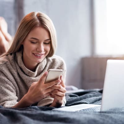 A woman looking at her phone in bed in a well-lit bedroom at Ocotillo Heights in Twentynine Palms, California