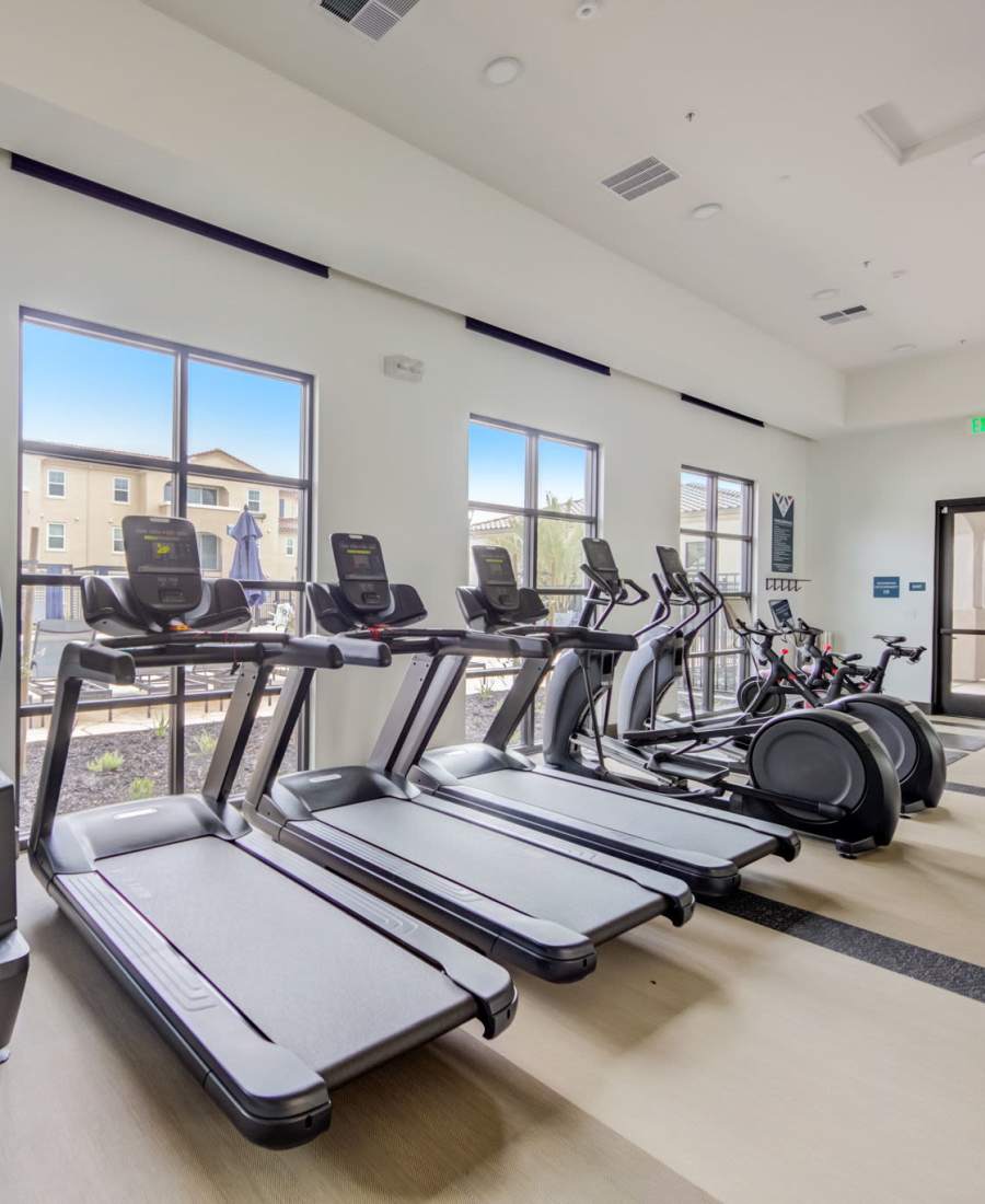 Apartments For Rent In Mountain House, CA - Aviara At Mountain House - Fitness Center With Ceiling Fan, Exercise Equipment, Yoga Mats, And Windows.