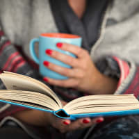 A woman holding a mug and reading at Cypress McKinney Falls in Austin, Texas