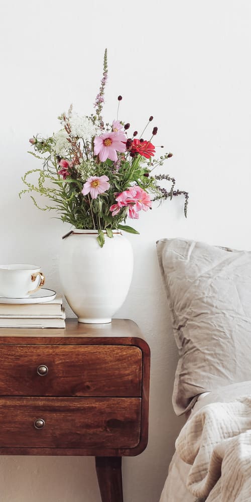 A modern side table with a colorful bouquet of flowers next to bed and decorative throw pillow