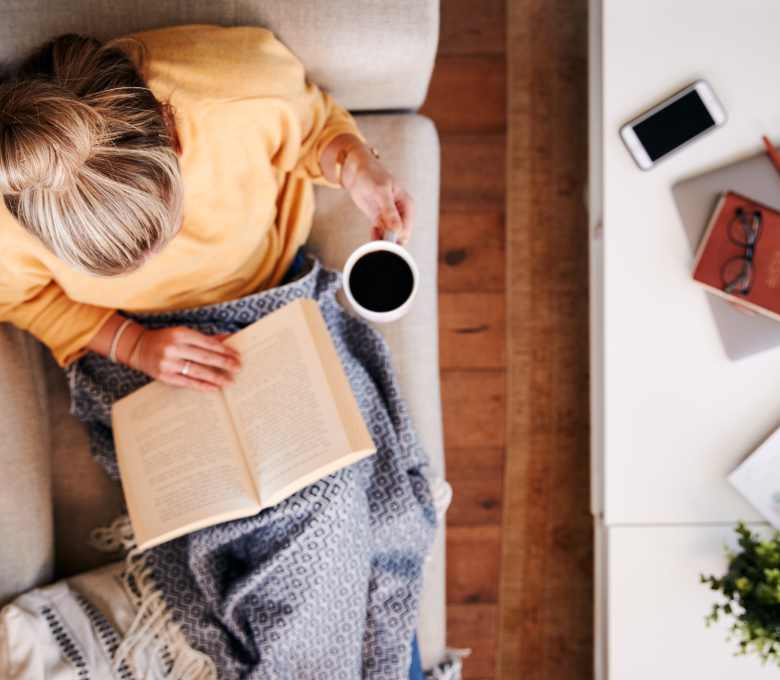 A woman reading a book while sitting on the couch drinking a cup of coffee Flatiron District at Austin Ranch, The Colony, Texas.