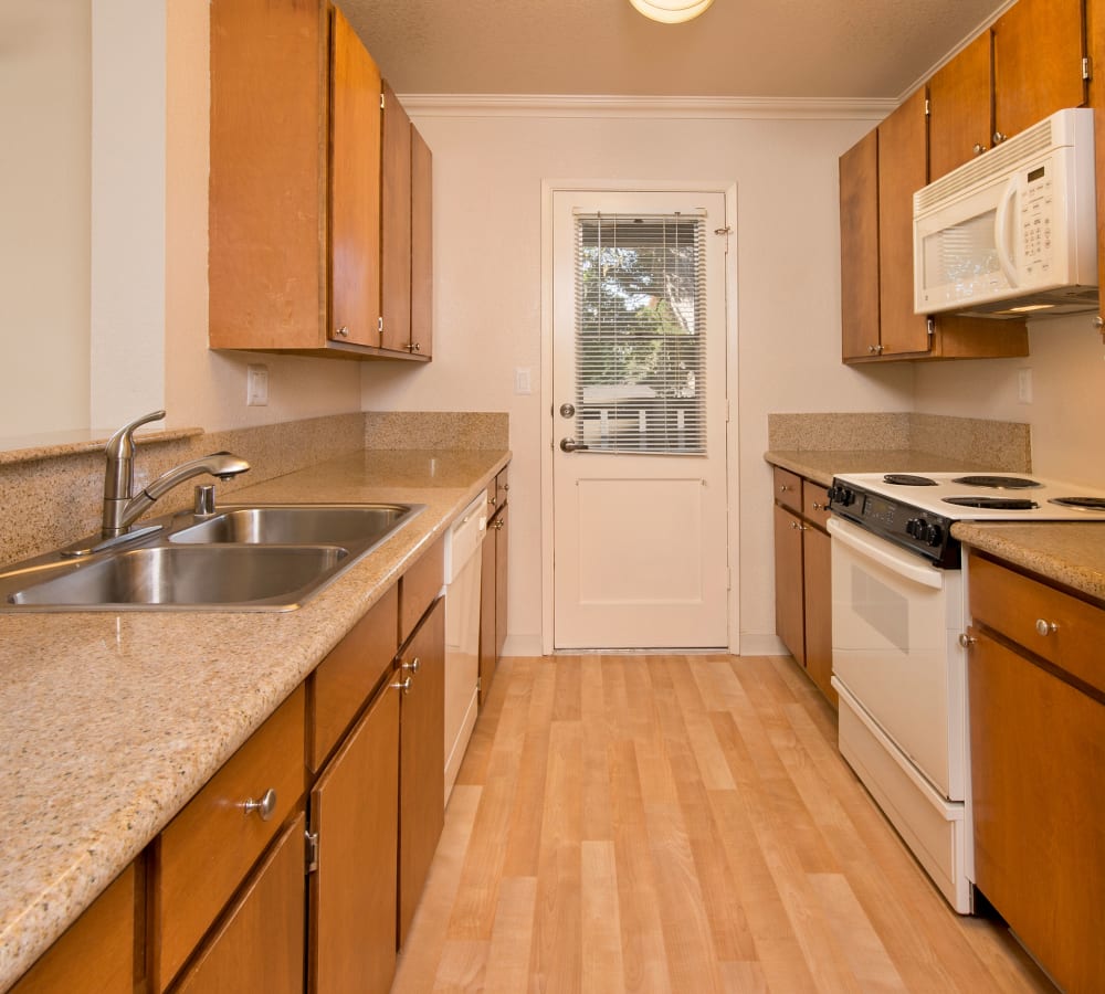Kitchen with wood-style cabinets and white appliances at Seventeen Mile Drive Village Apartment Homes in Pacific Grove, California