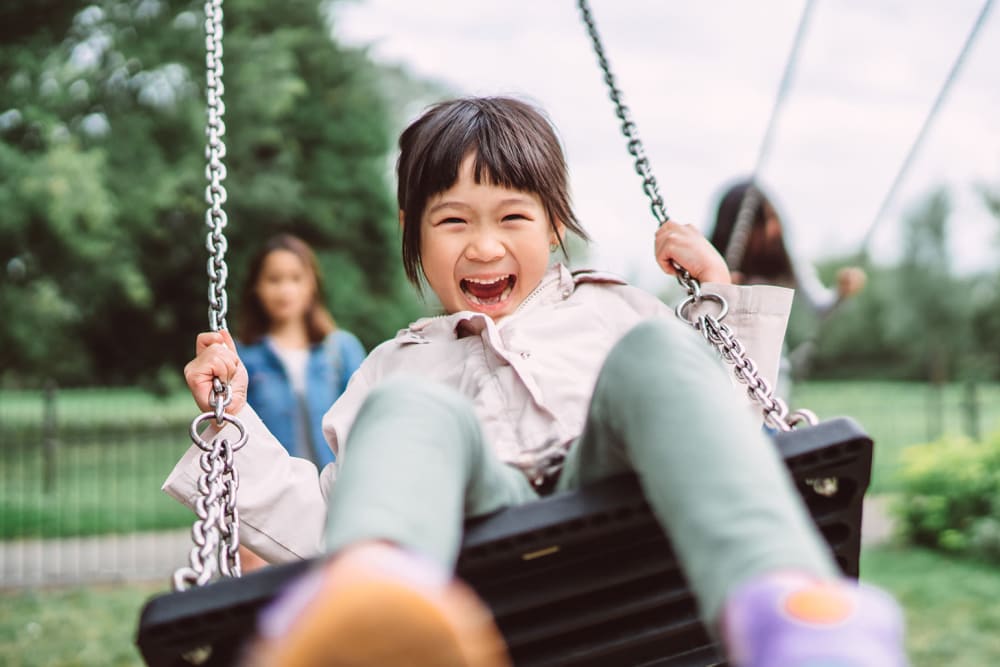 A smiling girl on a playground swing at Countrywood at Vernon in Vernon, Connecticut