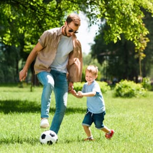 Father and son playing with a soccer ball in a park near Royalton Village in Hewitt, Texas