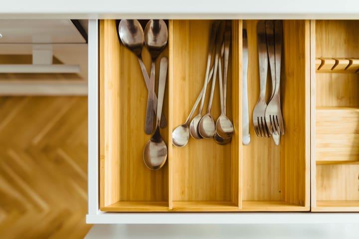 An open silverware drawer with forks, knives, and spoons organized in bamboo organizers