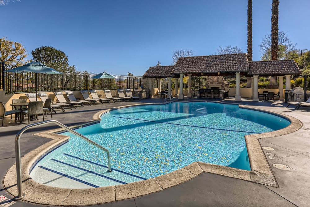 Spacious sundeck with table and chairs next to a swimming pool at Shadow Ridge Apartment Homes in Simi Valley, California