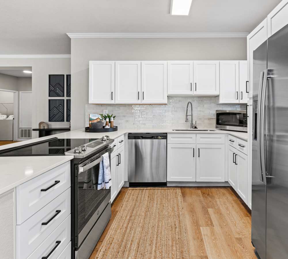 Kitchen with white cabinets, stone counters, stainless steel appliances & wood-style flooring.