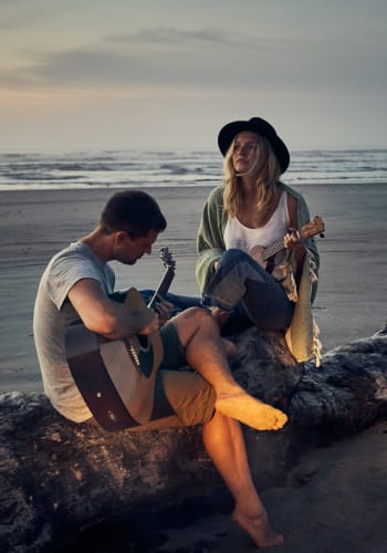 2 people sitting by the beach playing guitar at Artisan at East Village Apartments in Oxnard, California