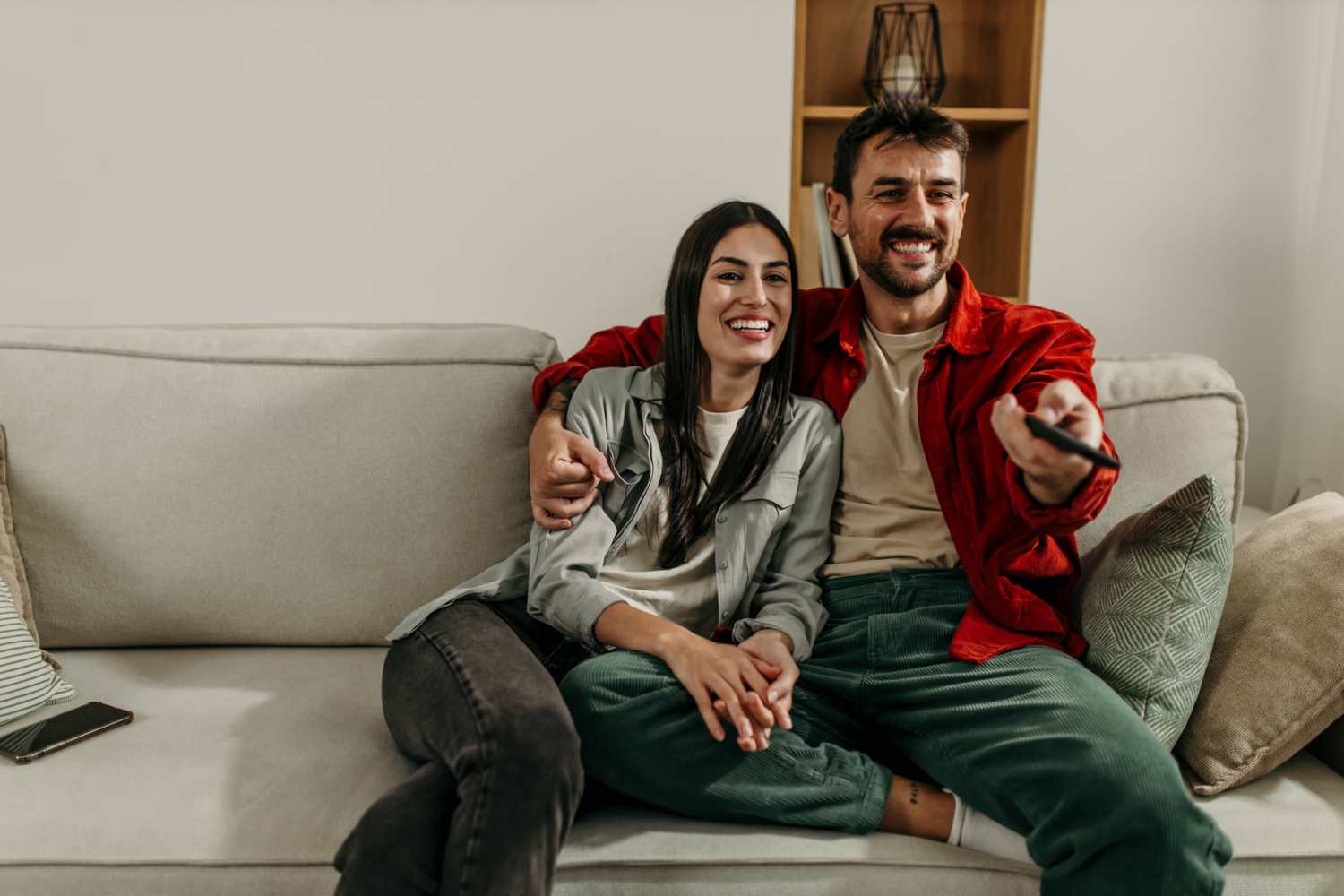A happy couple watching TV while sitting on a couch at Copper Hills Apartments in Houghton, Michigan