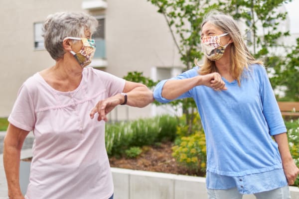 Senior ladies in masks touching elbows