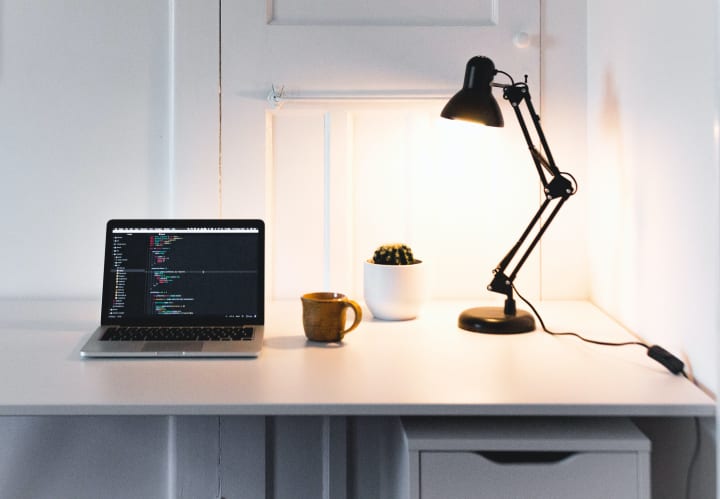 a desk lamp on a desk with an open laptop and a mug