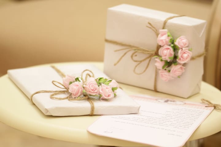 two ornately wrapped wedding presents in white paper with brown twine and pink paper mache roses