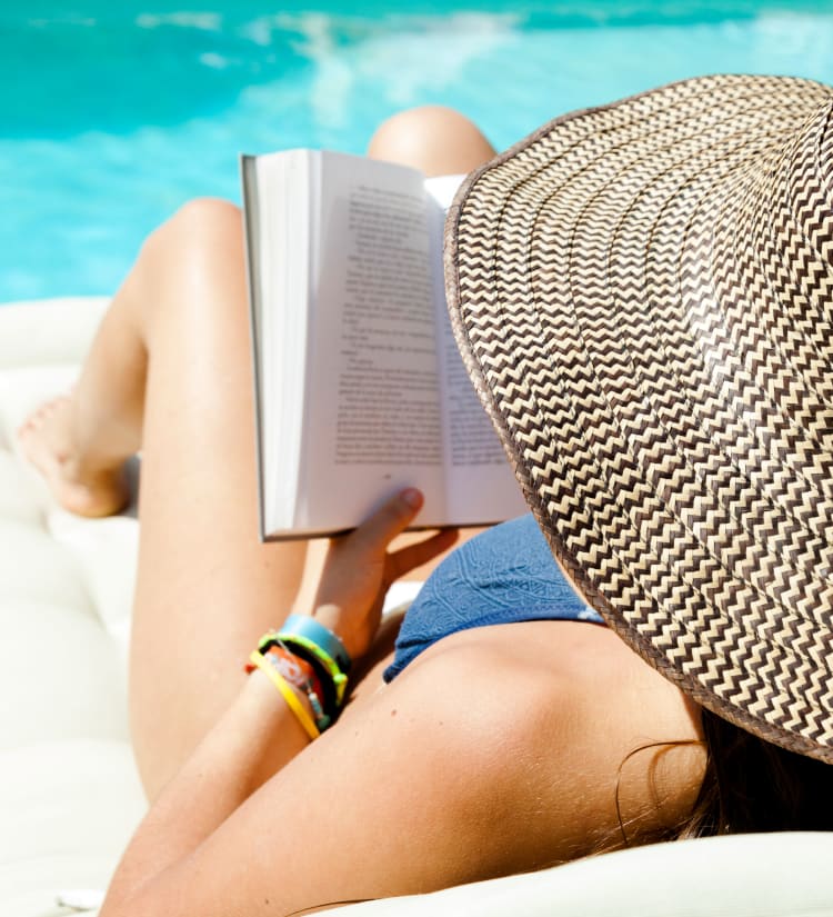 Resident reading a book on a chaise lounge chair by the swimming pool at Magnolia on the Green in Allen, Texas
