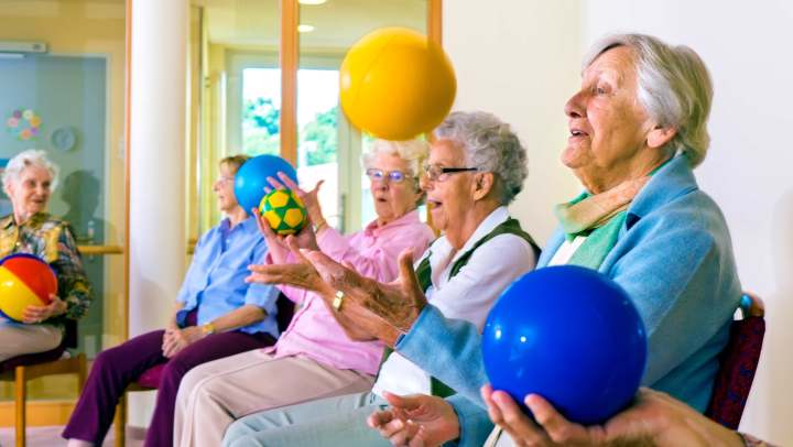 Elderly residents sitting on chairs doing a ball exercise.