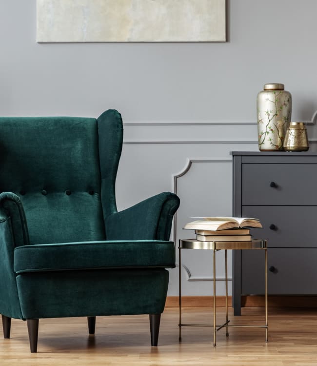 Beautiful emerald green velvet chair with a side table, gold vase and chests of drawers at Estoria Cooperative Lakeville in Lakeville, Minnesota